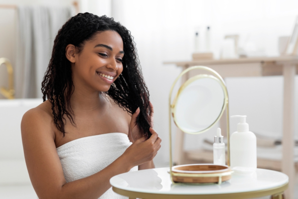 Frau mit lockigem Haar blickt in einen Kosmetikspiegel.